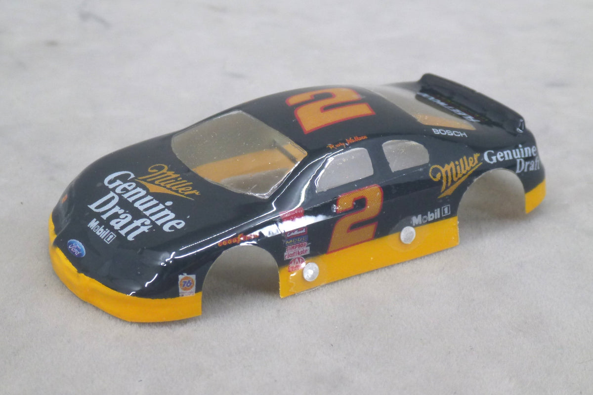 A lexan race car body shell in black with yellow and orange Miller Genuine Draft livery, featuring the number 2 and sponsor logos, photographed on a light gray textured surface.