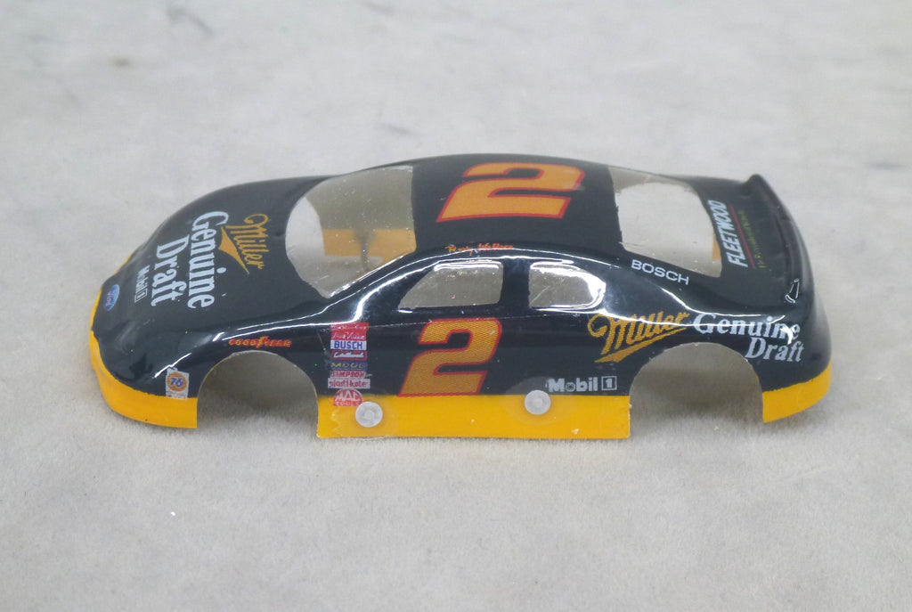 A black and yellow race car body shell with orange number 2 decals and sponsor logos, photographed on a light gray textured surface.