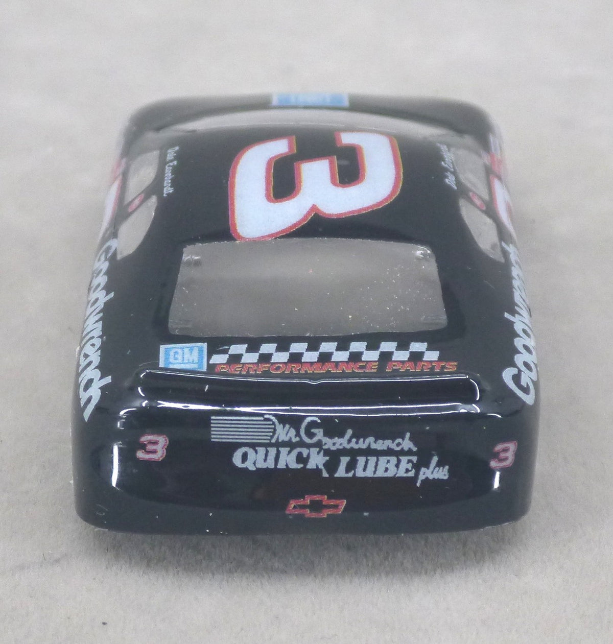 A black lexan model race car body shell featuring the number 3 and sponsor decals including Goodwrench, GM Performance Parts, and Mr. G's Quick Lube, photographed on a neutral gray background.