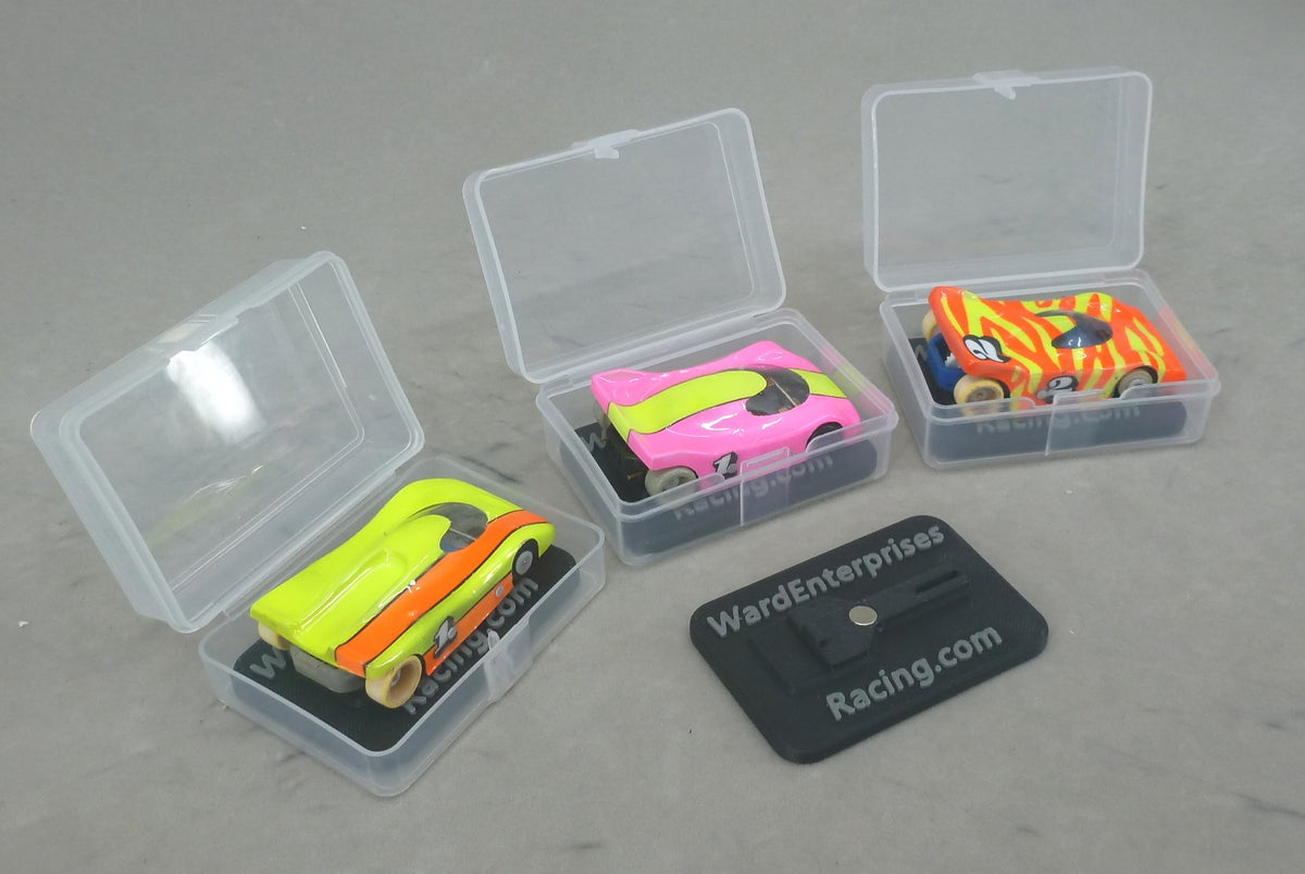 Three clear HO slot car cases with painted G Chassis cars on black chassis stands